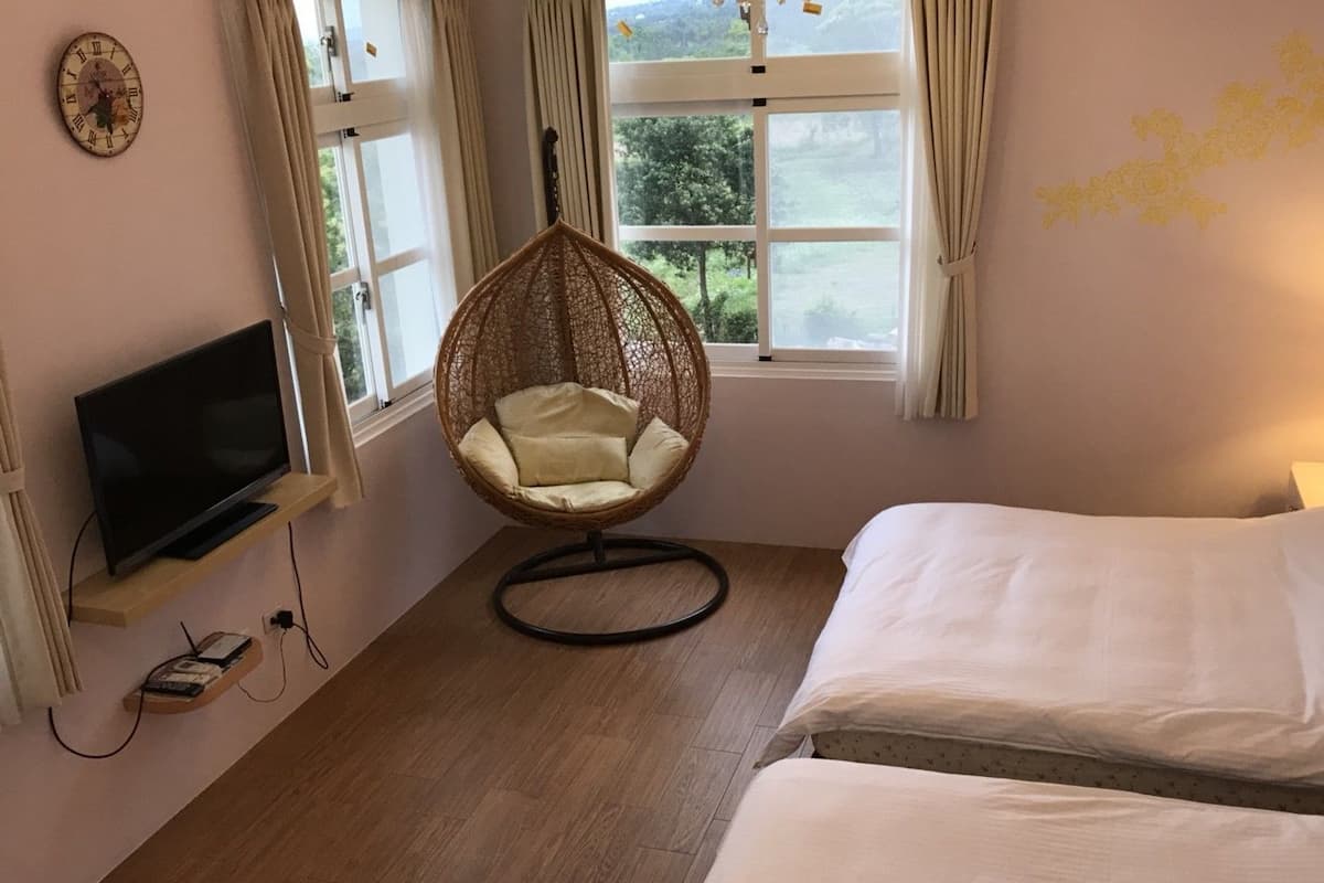 Un dormitorio con televisión en una estantería, una silla colgante, dos camas y un ventanal con cortinas.