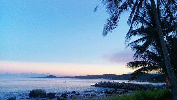 A beach with a rocky shoreline, palm trees, and a distant lighthouse. - Straybirds BnB (Donghe)