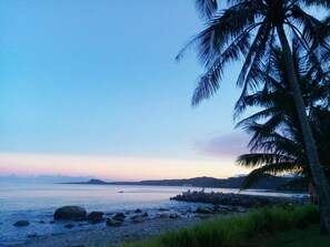 A beach with a rocky shoreline, palm trees, and a distant lighthouse. - Straybirds BnB (Donghe)