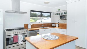 A modern kitchen with a stove, oven, sink, and wooden countertop. - Bucks Point House (Norfolk Island)