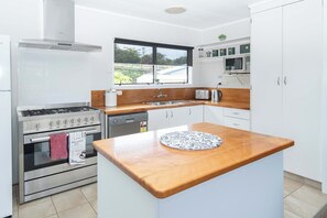 A modern kitchen with a stove, oven, sink, and wooden countertop. - Bucks Point House (Norfolk Island)