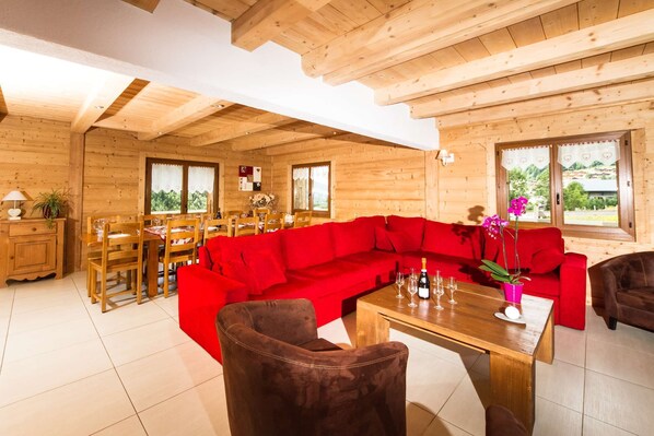 A wooden cabin interior with a red sofa, dining table, and chairs.