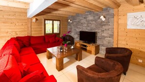 L’intérieur d’un chalet en bois chaleureux et accueillant, avec un canapé d’angle rouge, une table basse en bois et une cheminée en pierre.