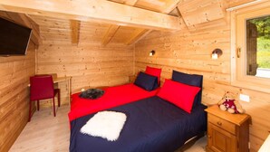 Une pièce de style cabane en bois, comprenant un lit, un bureau, une chaise et une fenêtre.