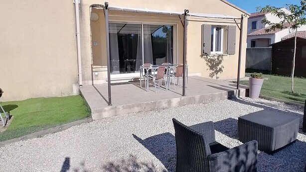 Un patio cubierto con mobiliario exterior, una puerta corrediza de vidrio y suelo de grava.