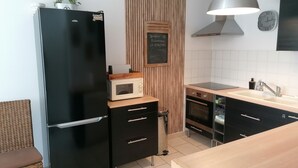Una cocina moderna con un refrigerador negro, un microondas, un panel de pared de madera, una pizarra con un saludo, un reloj y una lámpara colgante.