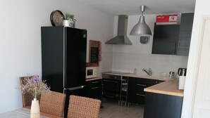 Una cocina moderna con un refrigerador negro, un microondas y un lavamanos. Hay un comedor con una mesa de madera y sillas de mimbre.