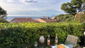 A glass table with two plates, a wine bottle, and a glass on a patio overlooking a coastal area with houses and greenery. - Apartment type villa in Sanary sea view, 150m from the beach with Jacuzzi plus parking (Sanary-sur-Mer)