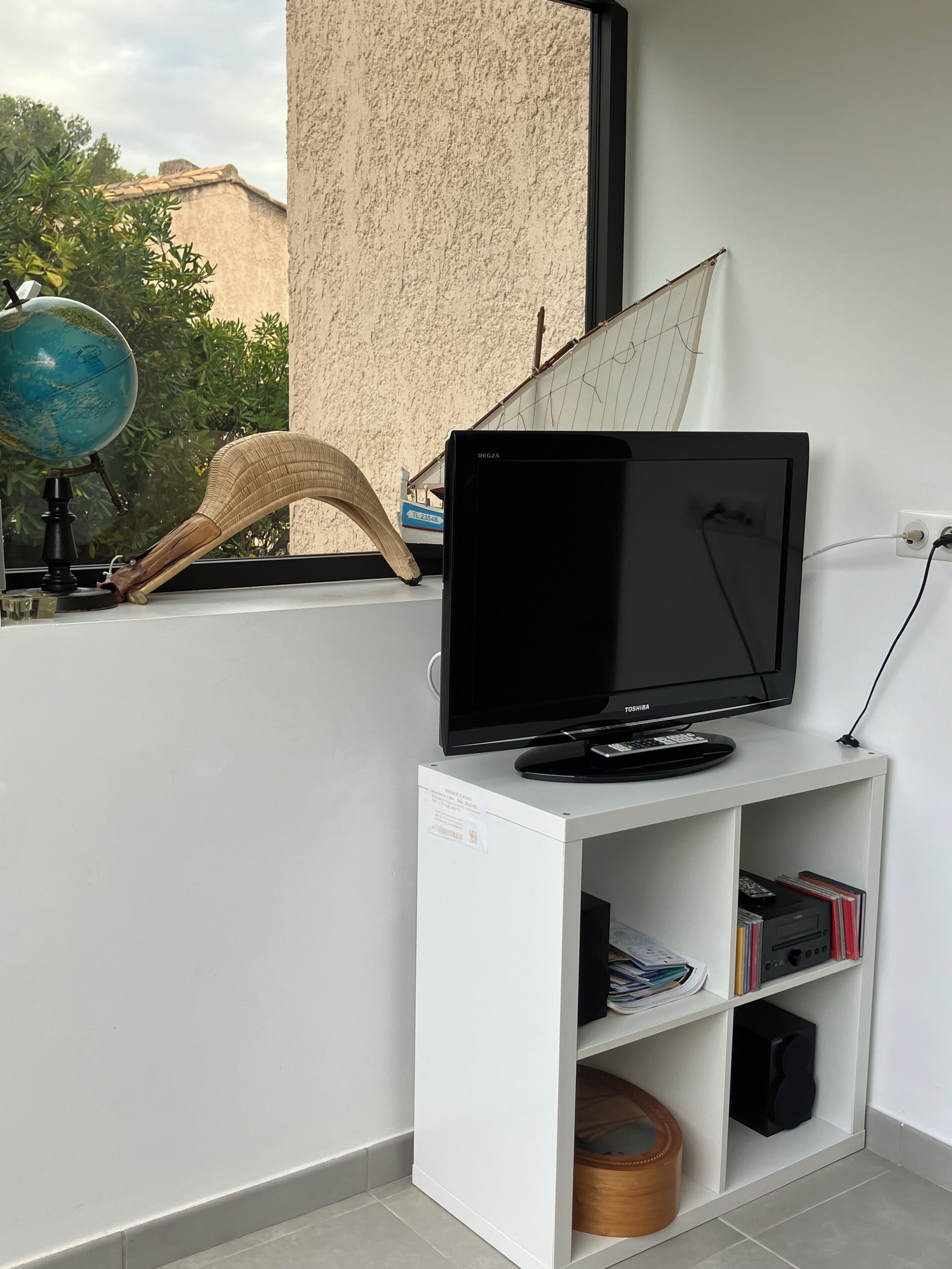 A flat-screen TV on a white shelf, a globe, and a woven basket on a balcony.
