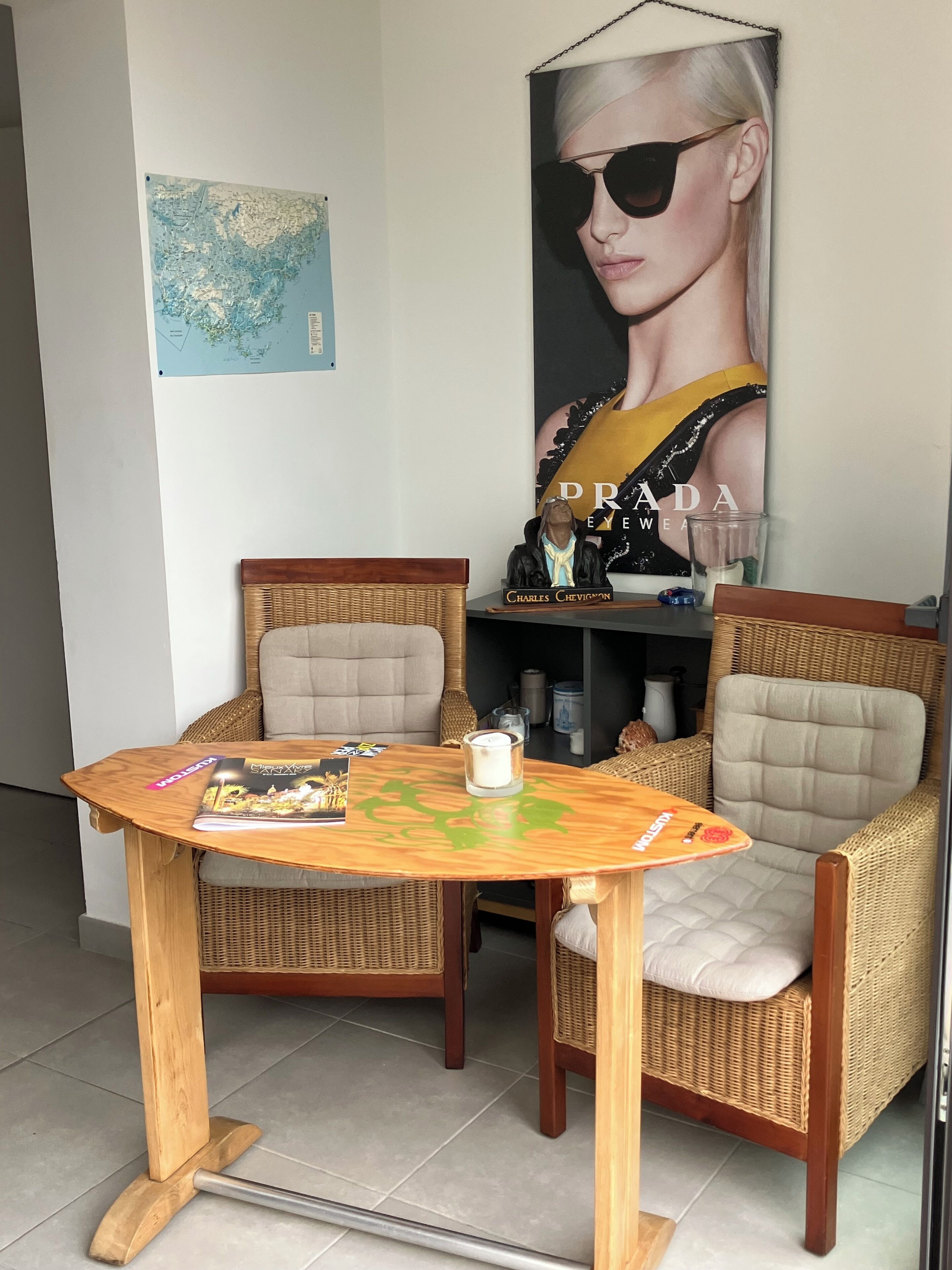 A room with wicker chairs, a wooden table, a map on the wall, and a large poster.
