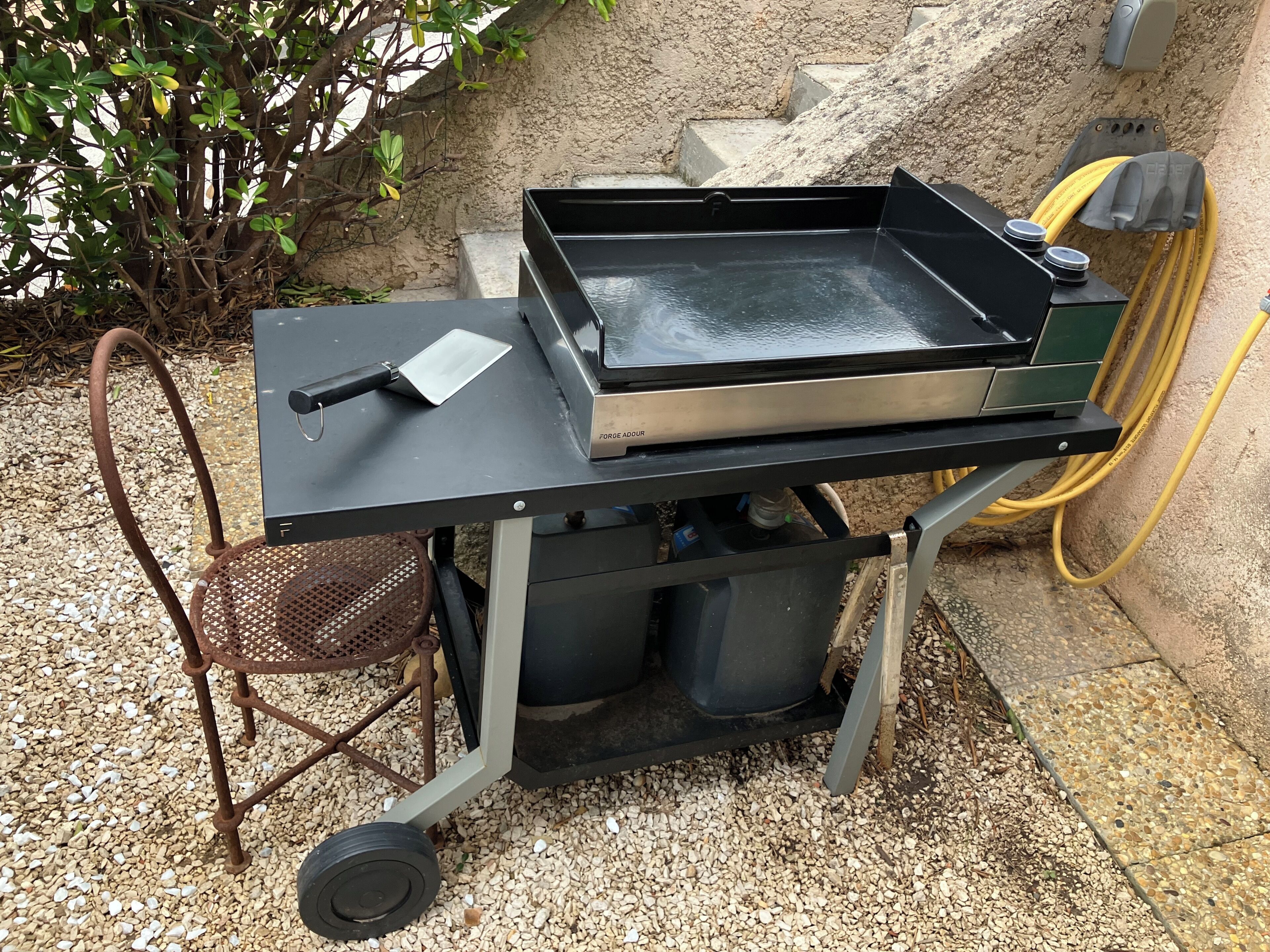 Un barbecue portable doté d’une surface de cuisson plane, d’une spatule et d’un récipient à eau.