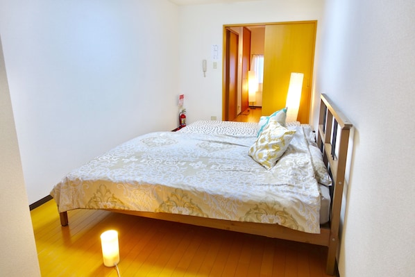 A neatly made bed with a patterned bedspread, a bedside lamp, and a fire extinguisher on the wall.