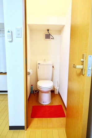 A compact bathroom with a white toilet, a red mat, and a small heater on the wall.