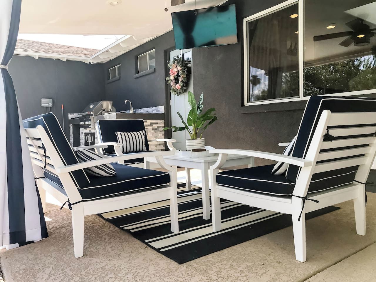 Un patio con sillas blancas y una mesa, una planta en maceta y vista a una casa con fachada oscura.