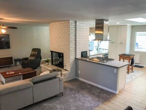 A modern kitchen with a central island, a built-in fireplace, and a dining area with a sofa and coffee table. - Pecos Lane | Poolside by Day, Wolf Den by Night (Scottsdale)