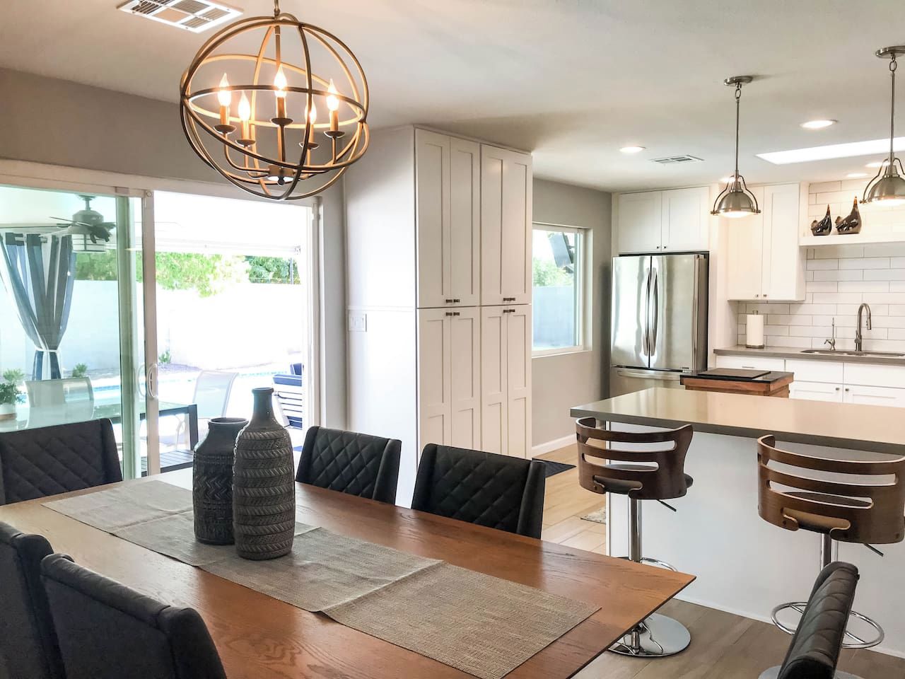 A modern kitchen with white cabinets, a stainless steel refrigerator, and pendant lighting.