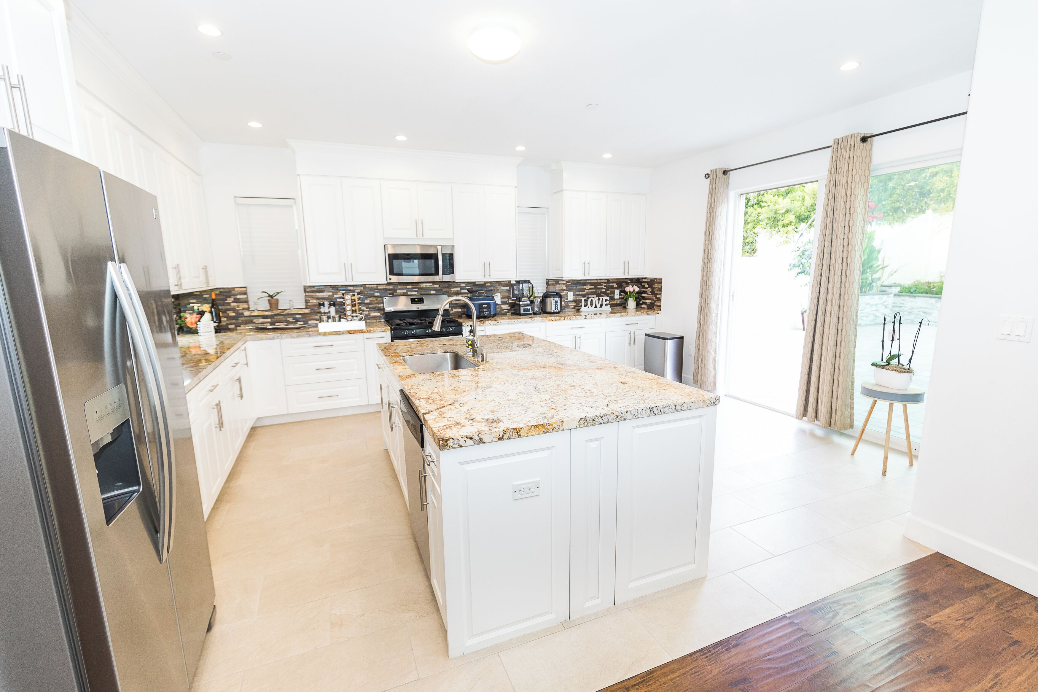 A modern kitchen with white cabinets, a granite countertop, stainless steel appliances, and a large island with a sink.
