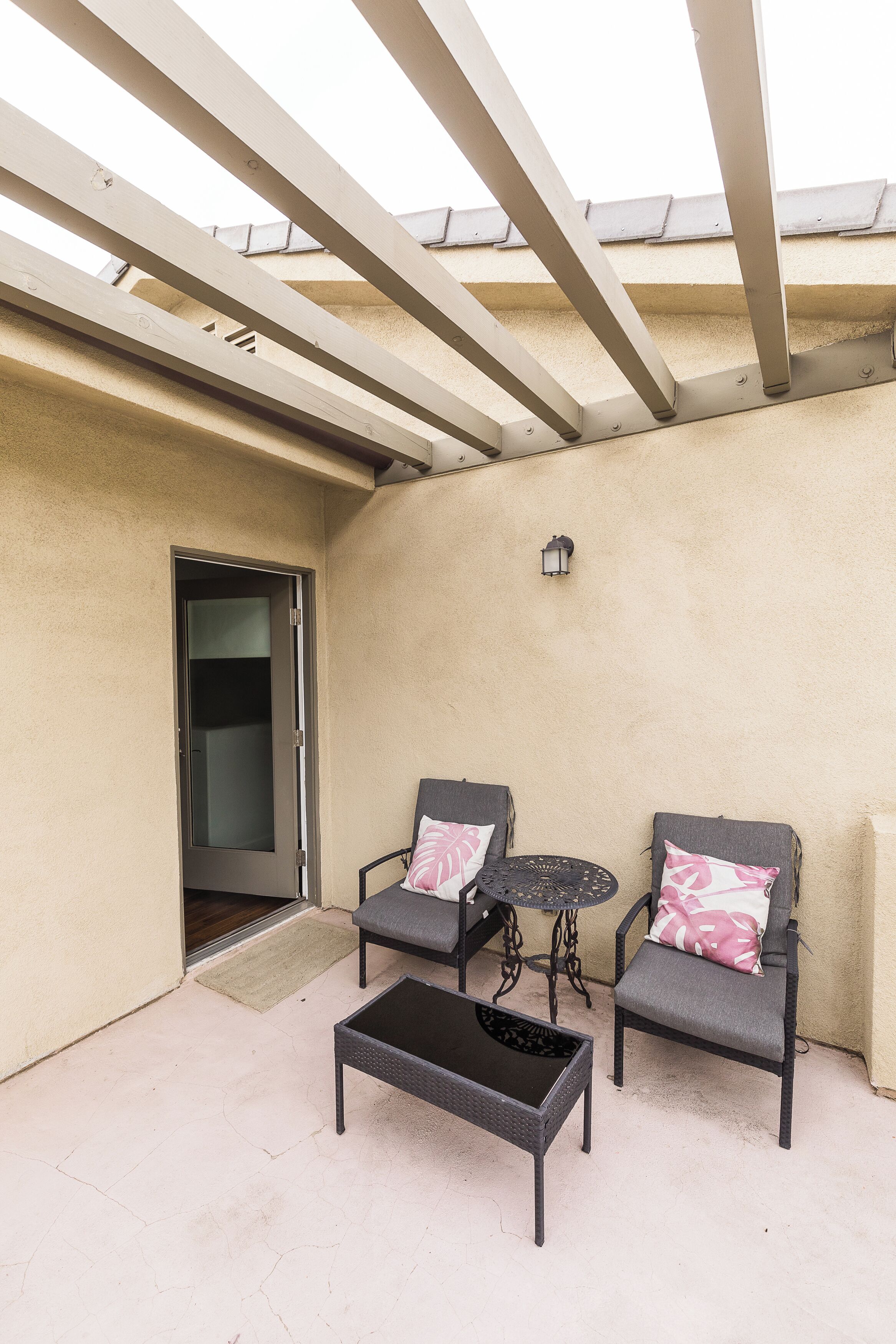 An outdoor patio with two chairs, a small table, and a door leading to an interior space.