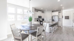 A modern kitchen with white cabinets, a central island, and a dining area with a round table and chairs. - Spacious 4BR Sleeps 12 - 2 Rec Rooms on the 18th (St. George)