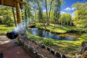 Een barbecue klaargezet in de buurt van een vijver met een houten brug in een weelderig, groen park.