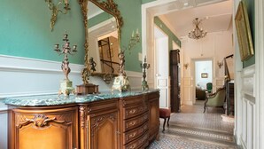 A grand hallway with a marble counter, ornate candelabras, and a large mirror.