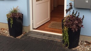 Una entrada residencial con puerta corredera de vidrio, buzón y dos macetas.