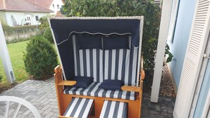Una silla de playa de madera con cojines a rayas y un toldo, ubicada en un patio empedrado.