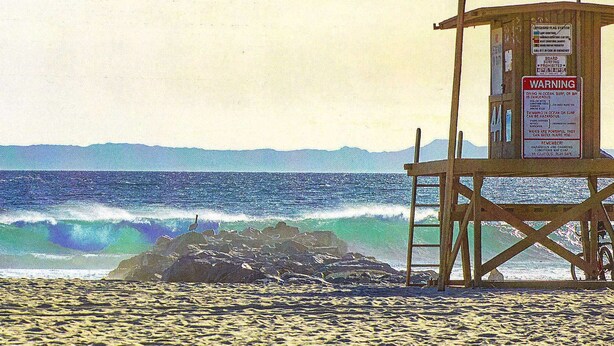 Una torre di salvataggio con cartelli di avvertimento, una spiaggia sabbiosa e l'oceano con le onde.
