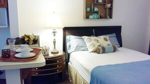 Camera d'albergo ordinata con un letto, un comodino, una lampada e un tavolino con tazze e un vaso.