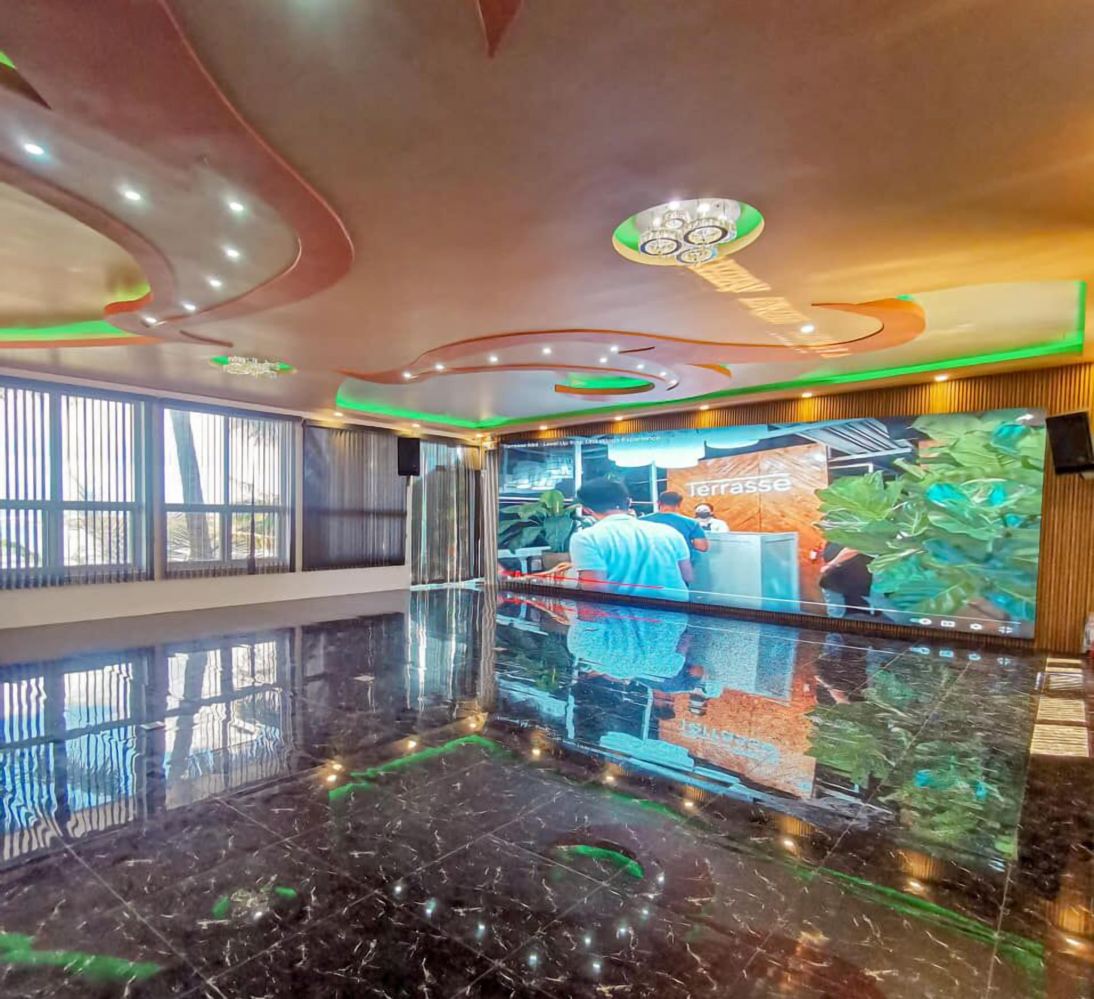 A lobby with a reflective marble floor, a large digital screen displaying a person working, and a 'Terrasse' sign.