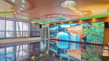 A lobby with a reflective marble floor, a large digital screen displaying a person working, and a 'Terrasse' sign.