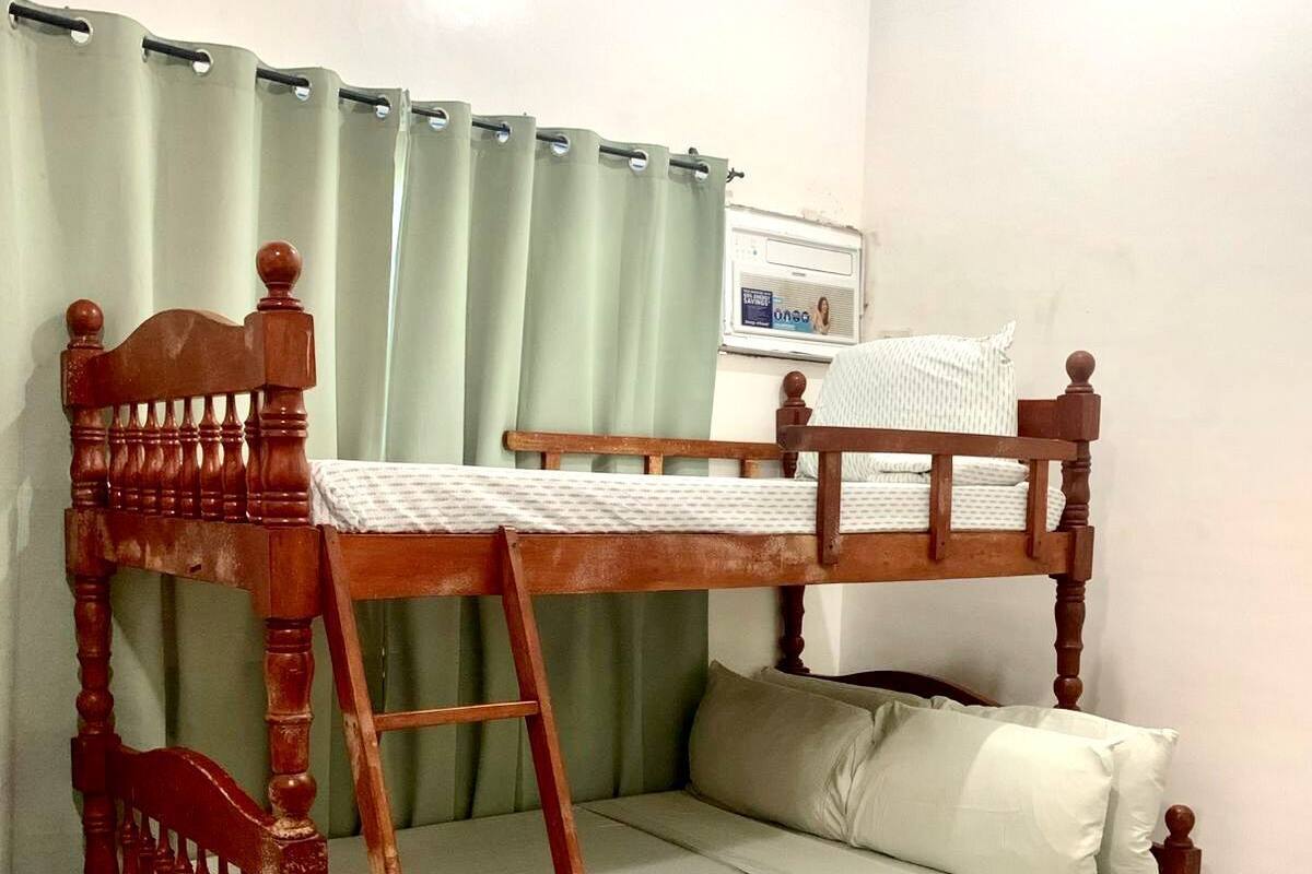 A bunk bed with a ladder, a small bedside table, and a window with a curtain.