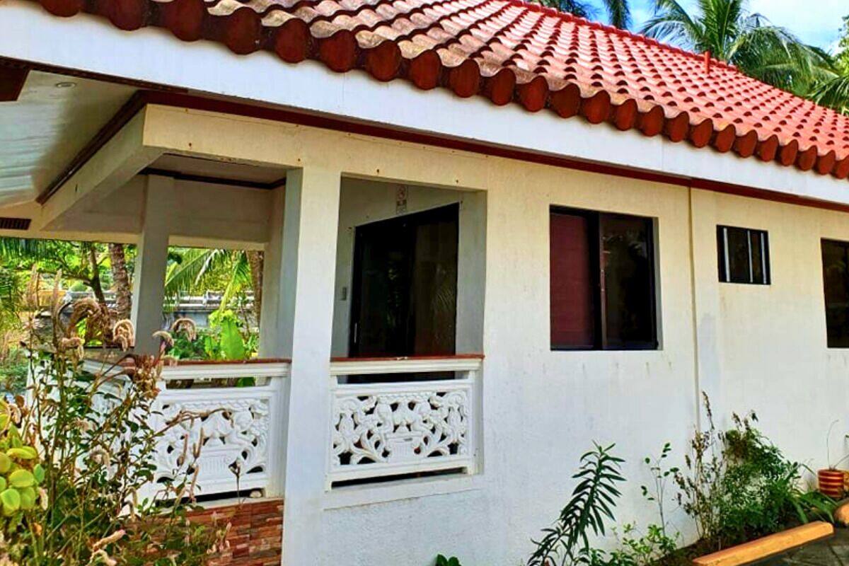 A single-story building with a red-tiled roof, white walls, and a covered porch with decorative railings.