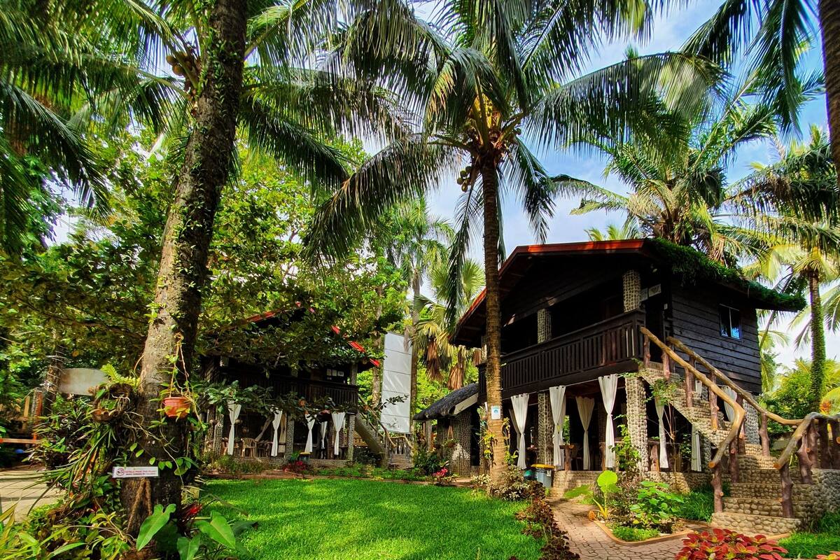 A tropical resort with a wooden building, palm trees, and a well-maintained garden.