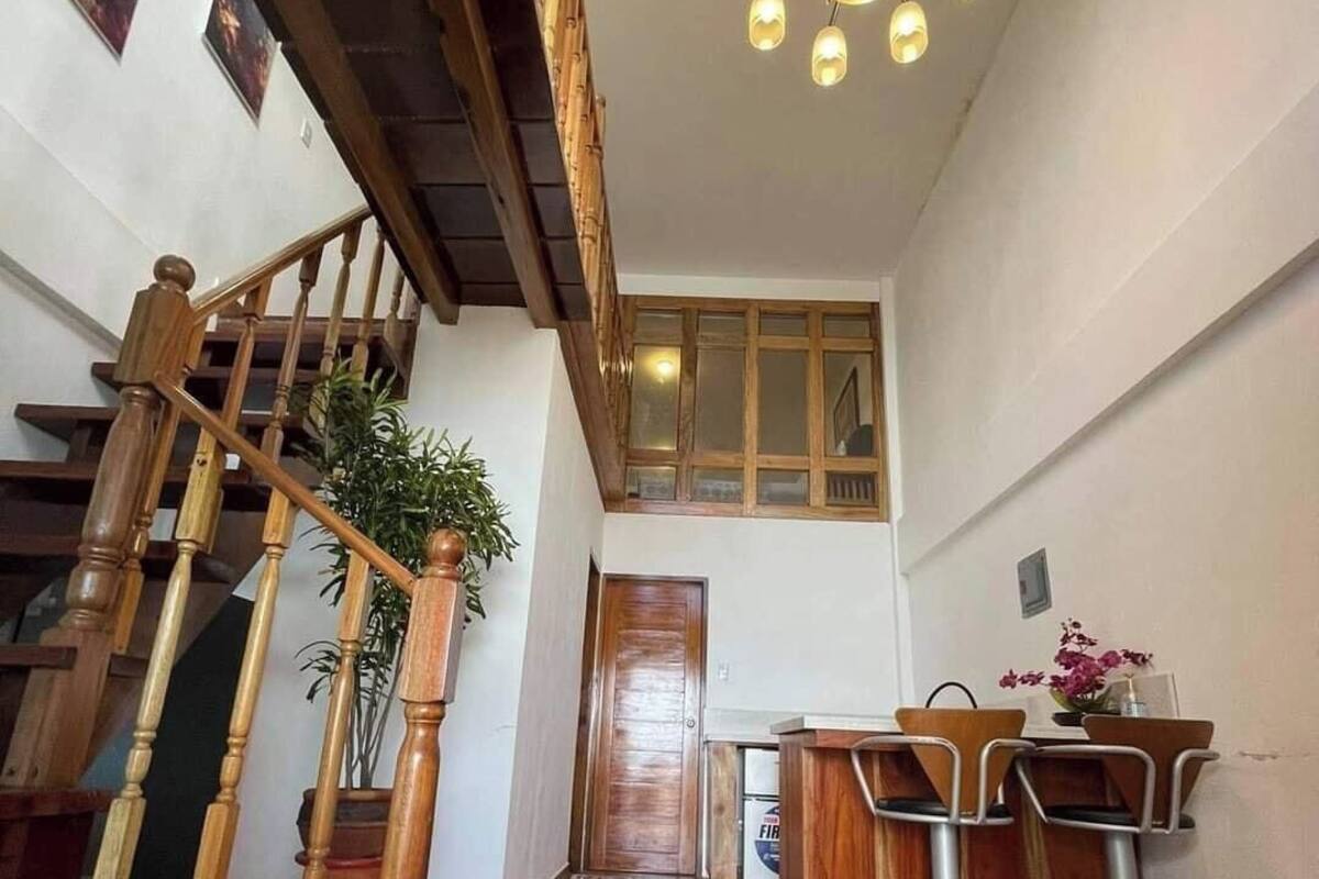 A wooden staircase leading to a second floor, a dining area with bar stools, and a chandelier.