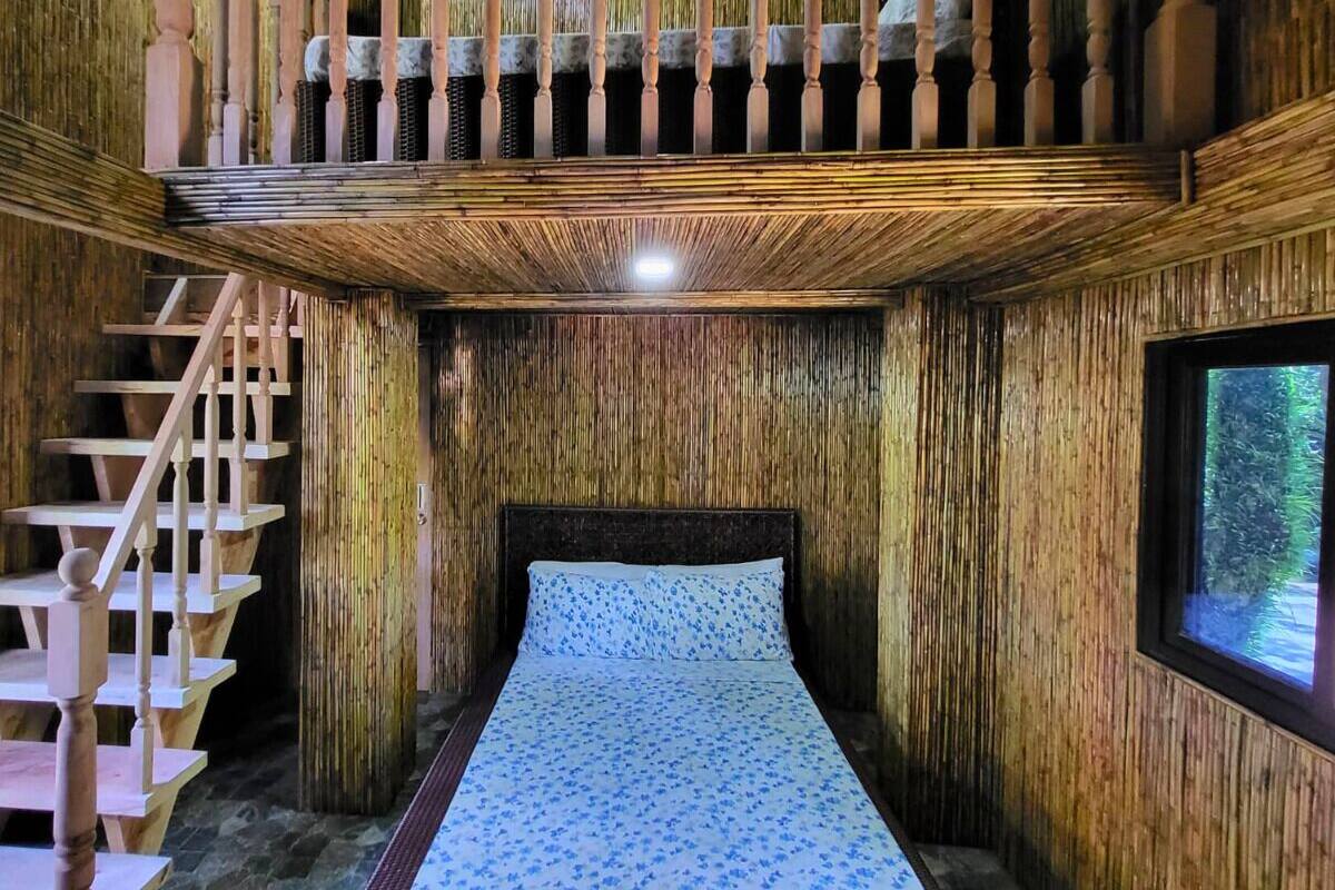 A bedroom with a wooden interior, a bed with a patterned bedspread, a window, and a wooden staircase.
