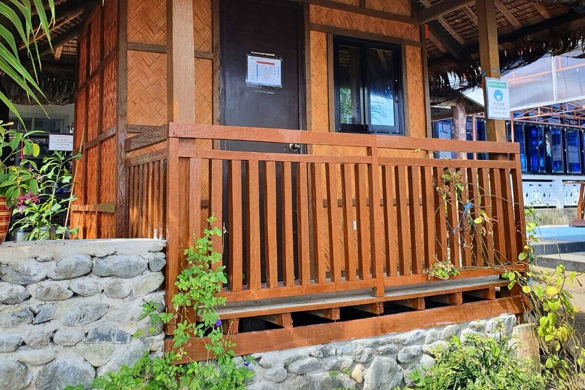 A wooden building with a thatched roof, a wooden porch, and a stone wall foundation.