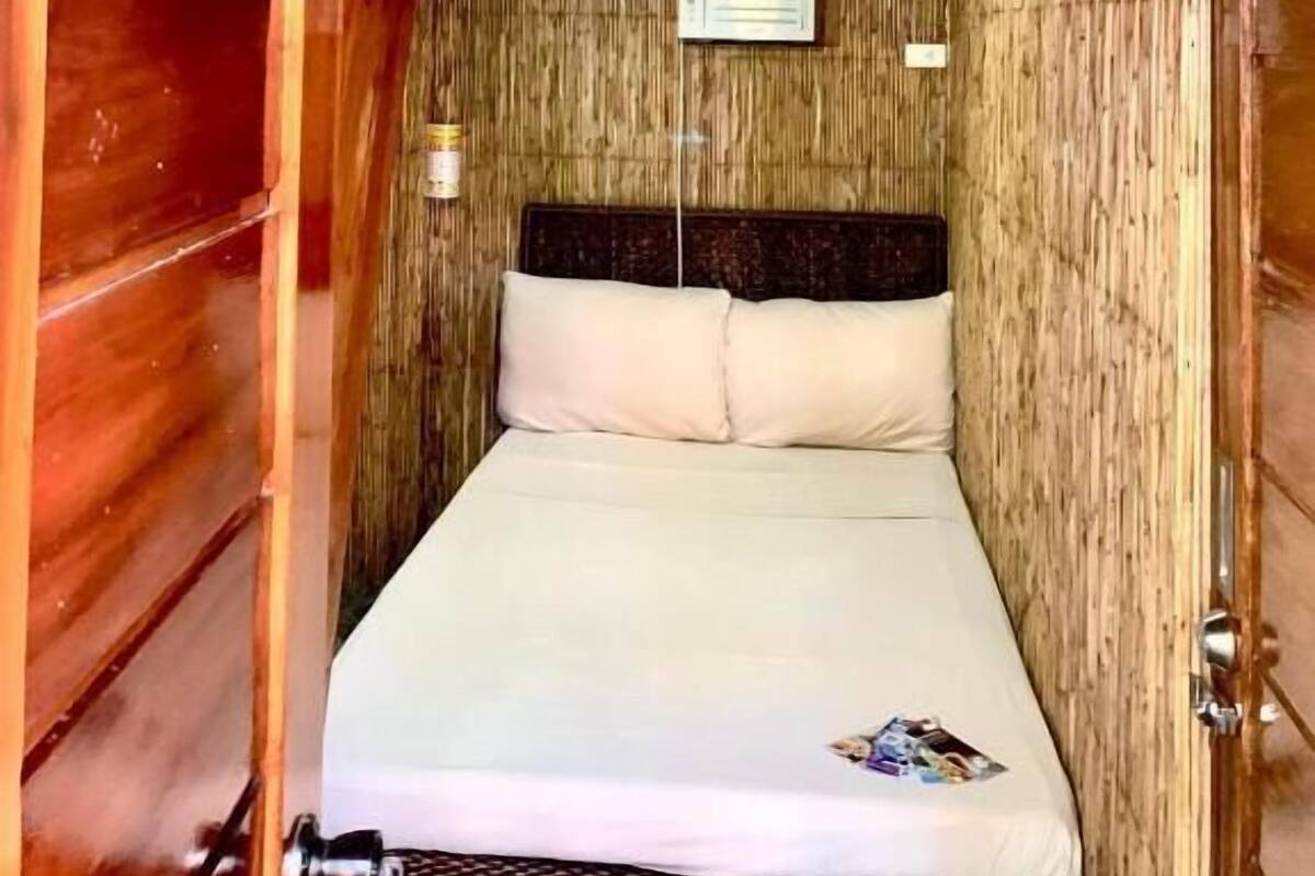 A compact room with a bunk bed, wooden walls, a small window, and a door.
