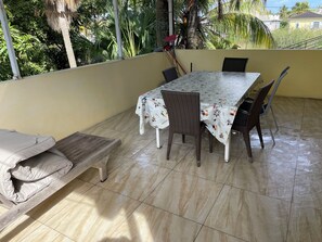An outdoor patio with a table and chairs, a bench, and a view of greenery and buildings.
