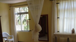 A room with a bed, a chair, a table, and a window with curtains.