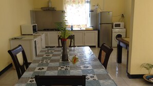 A compact kitchen with a dining table, chairs, a microwave, a refrigerator, and a washing machine.
