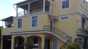 A two-story yellow building with a balcony, a covered porch, and a staircase.