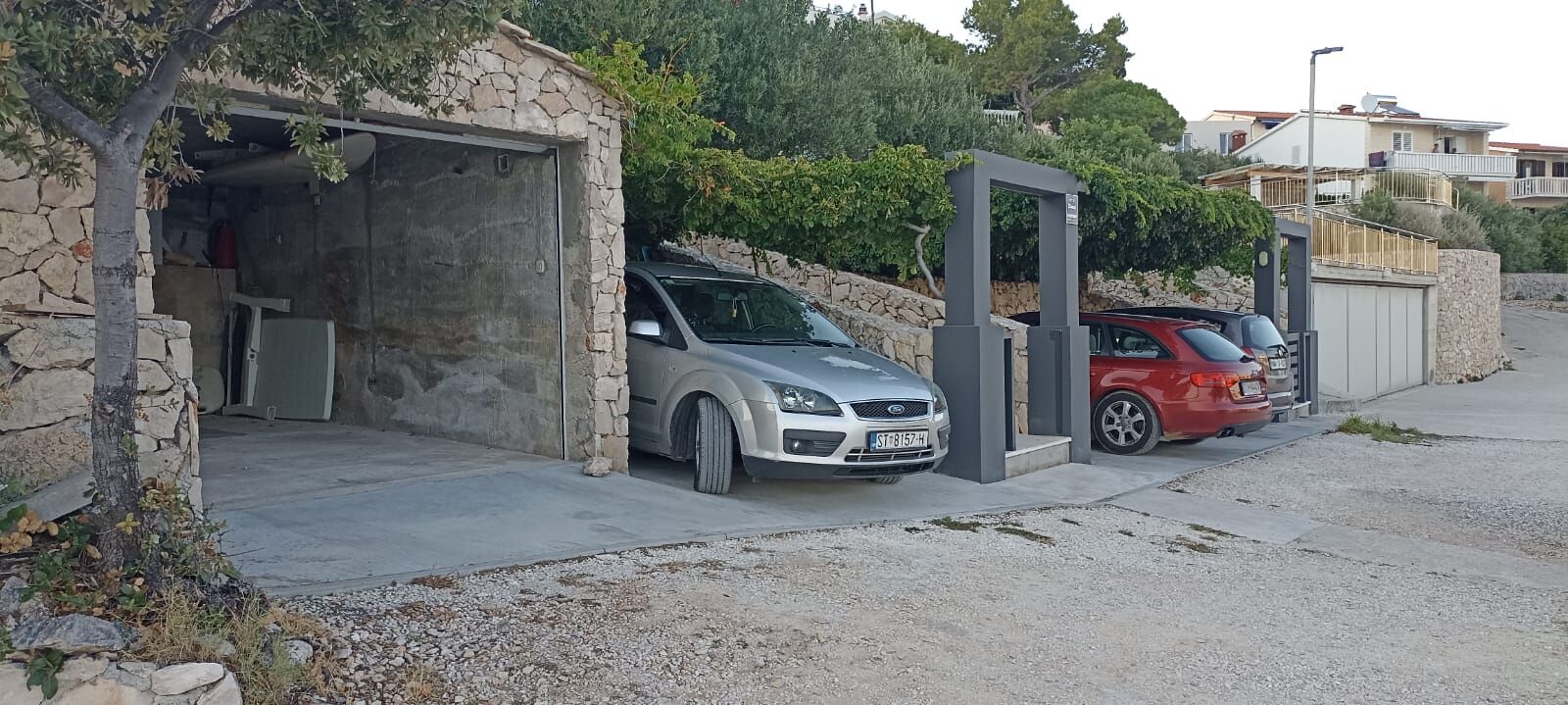 Uma área de estacionamento com dois carros estacionados perto de um muro de pedra e uma entrada coberta.