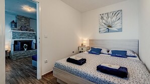 A bedroom with a bed, a nightstand, a wall-mounted lamp, a fireplace, and a large flower painting. - Cozy home in Potomje with WiFi (Potomje)
