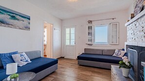 A modern living room with two sofas, a small table with a lamp, a fireplace, and a view of the sea through the windows. - Cozy home in Potomje with WiFi (Potomje)