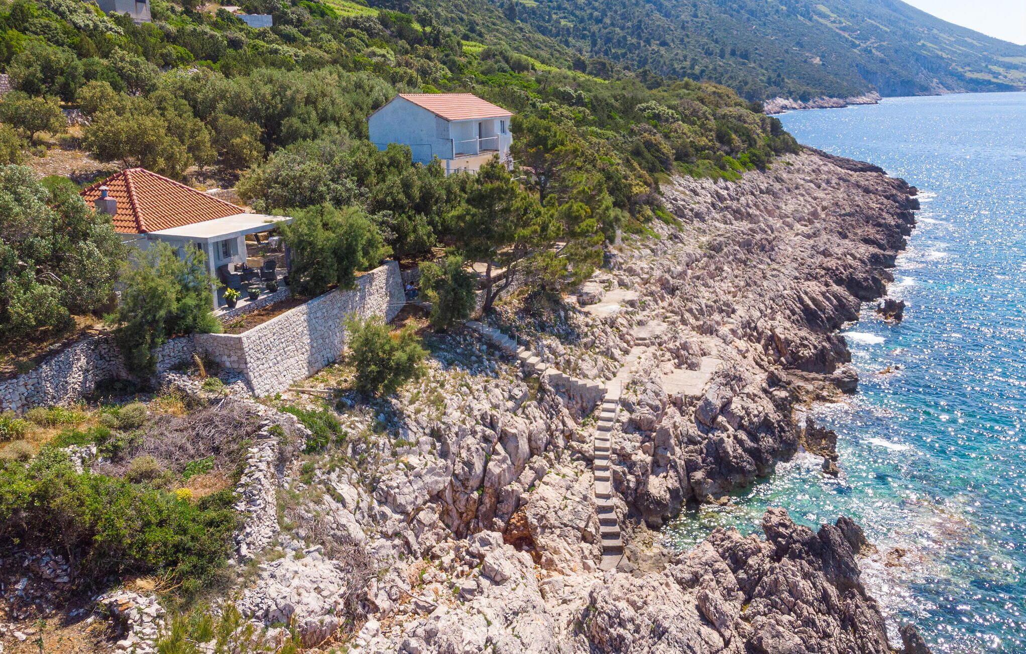 Una proprietà costiera con un muro in pietra, una piccola casa con tetto in tegole e vista libera sul mare.