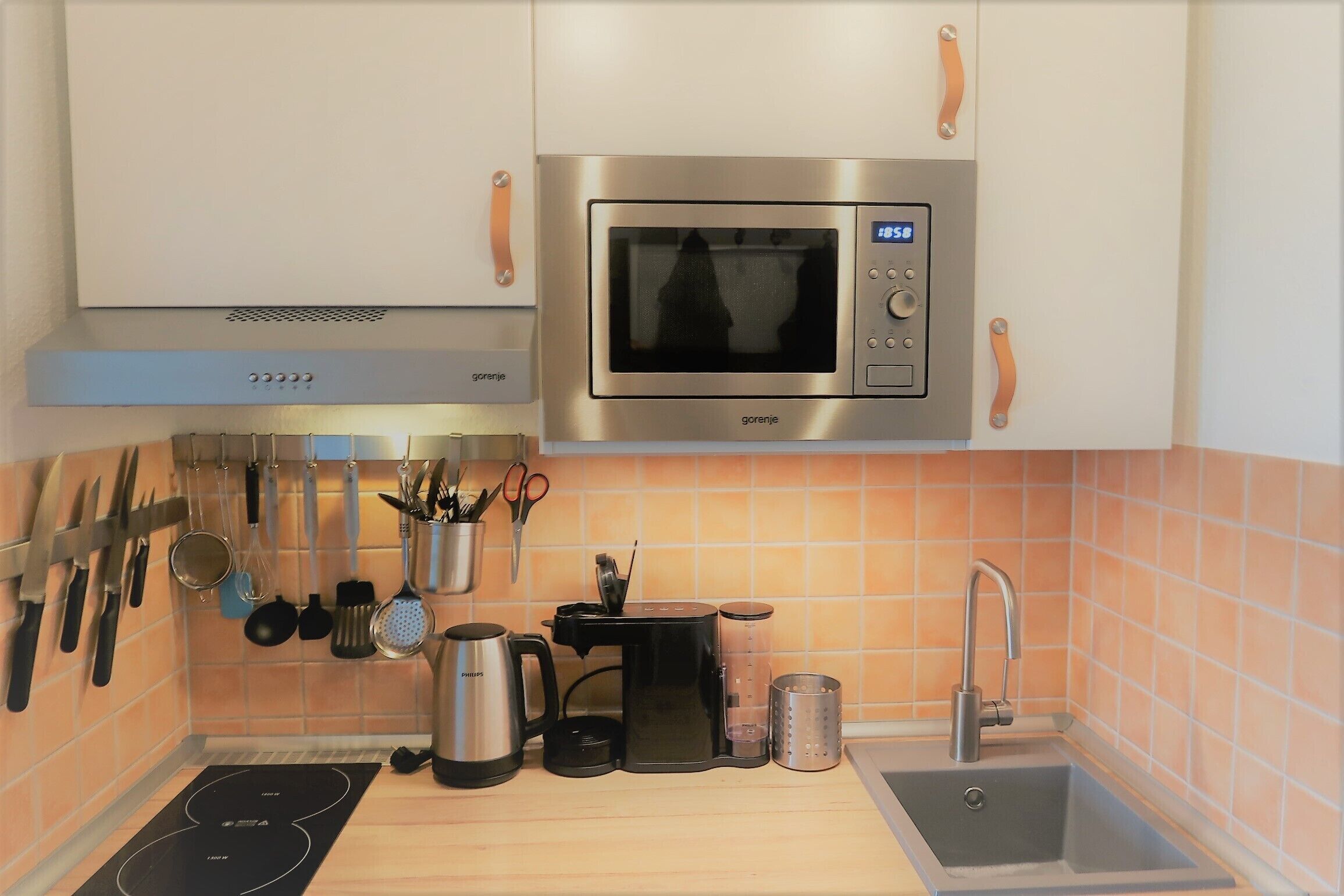 Une cuisine compacte équipée d’un four à micro-ondes encastré, d’une machine à café, d’une bouilloire et d’un évier.