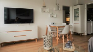 A modern living room with a flat-screen TV, a dining table with chairs, a white cabinet, and a glass coffee table. - Newly renovated apartment, lake view, directly on the south beach, WLAN & beach chair included (Burg auf Fehmarn)