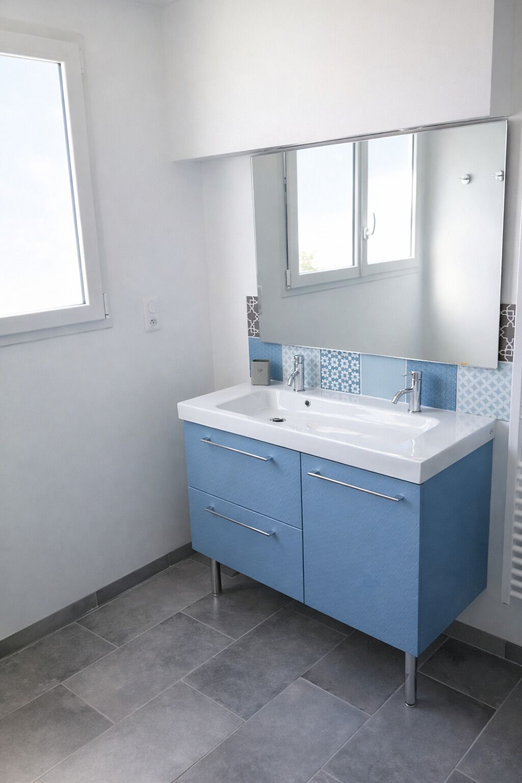Ein Badezimmer mit einem weißen Waschbecken, blauen Schränken und einem Fenster.