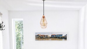 En matplats med ett träbord och sex grå stolar, en hängande lampa och en inramad tavla på väggen.